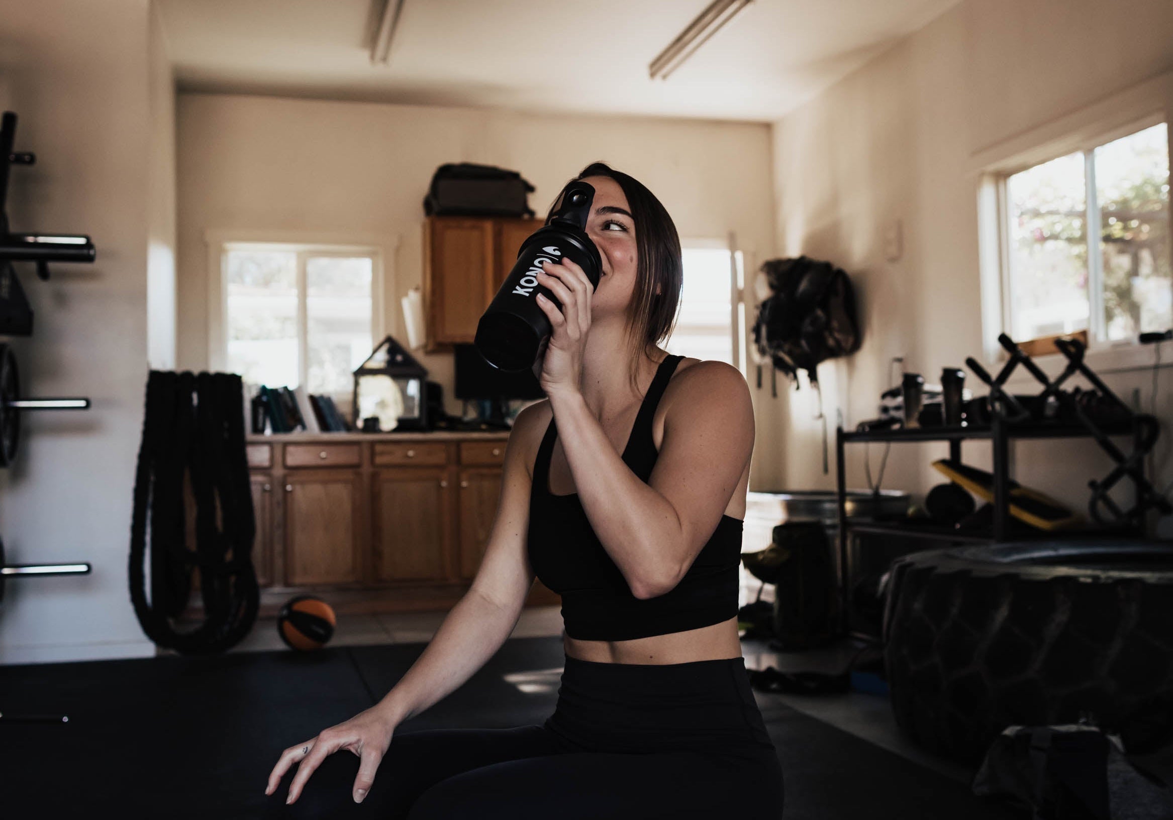 gym lifestyle photo—female athlete hydrating with KONO shaker while resting on a medicine ball