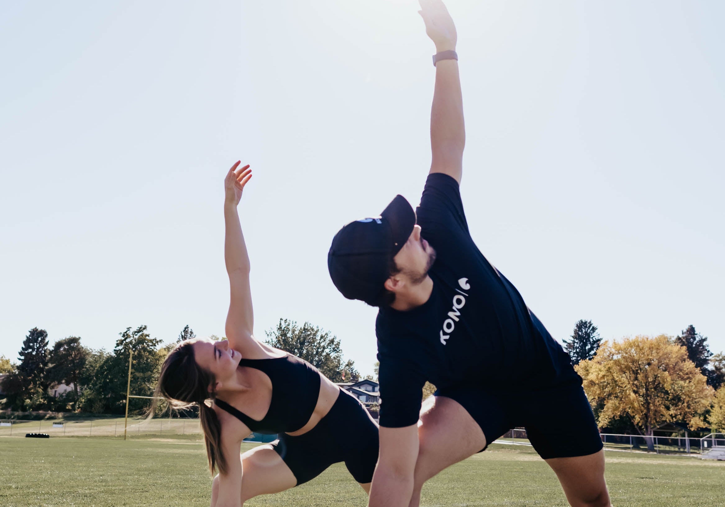 outdoor flexibility training—man and woman stretching side-to-side on a sports field under clear sky