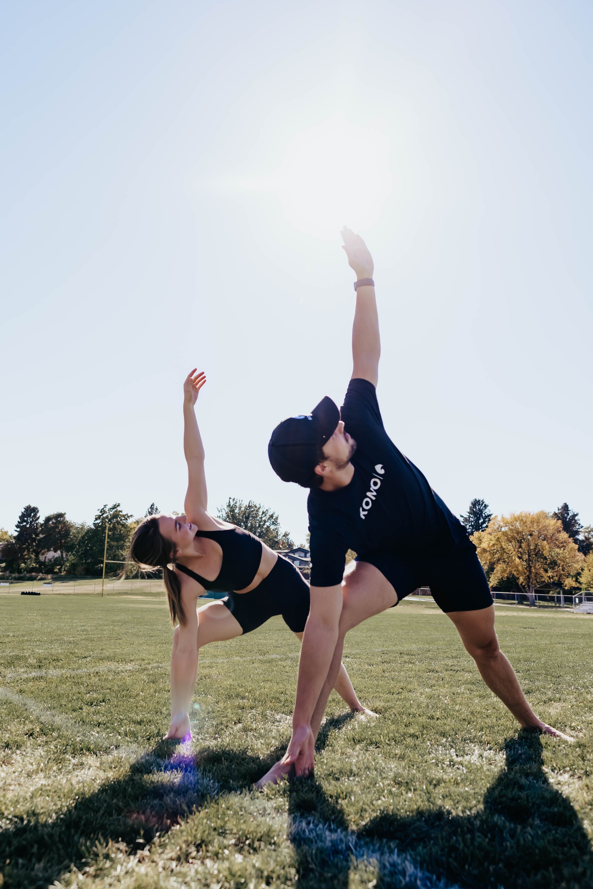 outdoor flexibility training—man and woman stretching side-to-side on a sports field under clear sky