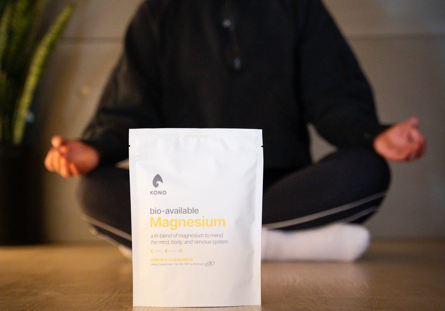 KONO bio-available magnesium pouch (lemon & chamomile) in focus while a person meditates cross-legged in the background
