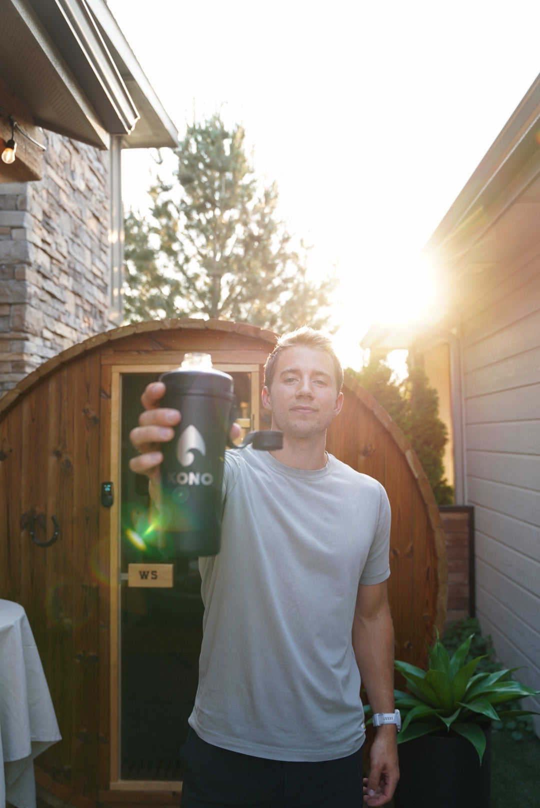 recovery scene: KONO shaker raised outside a sauna, casual t-shirt and sunburst in background