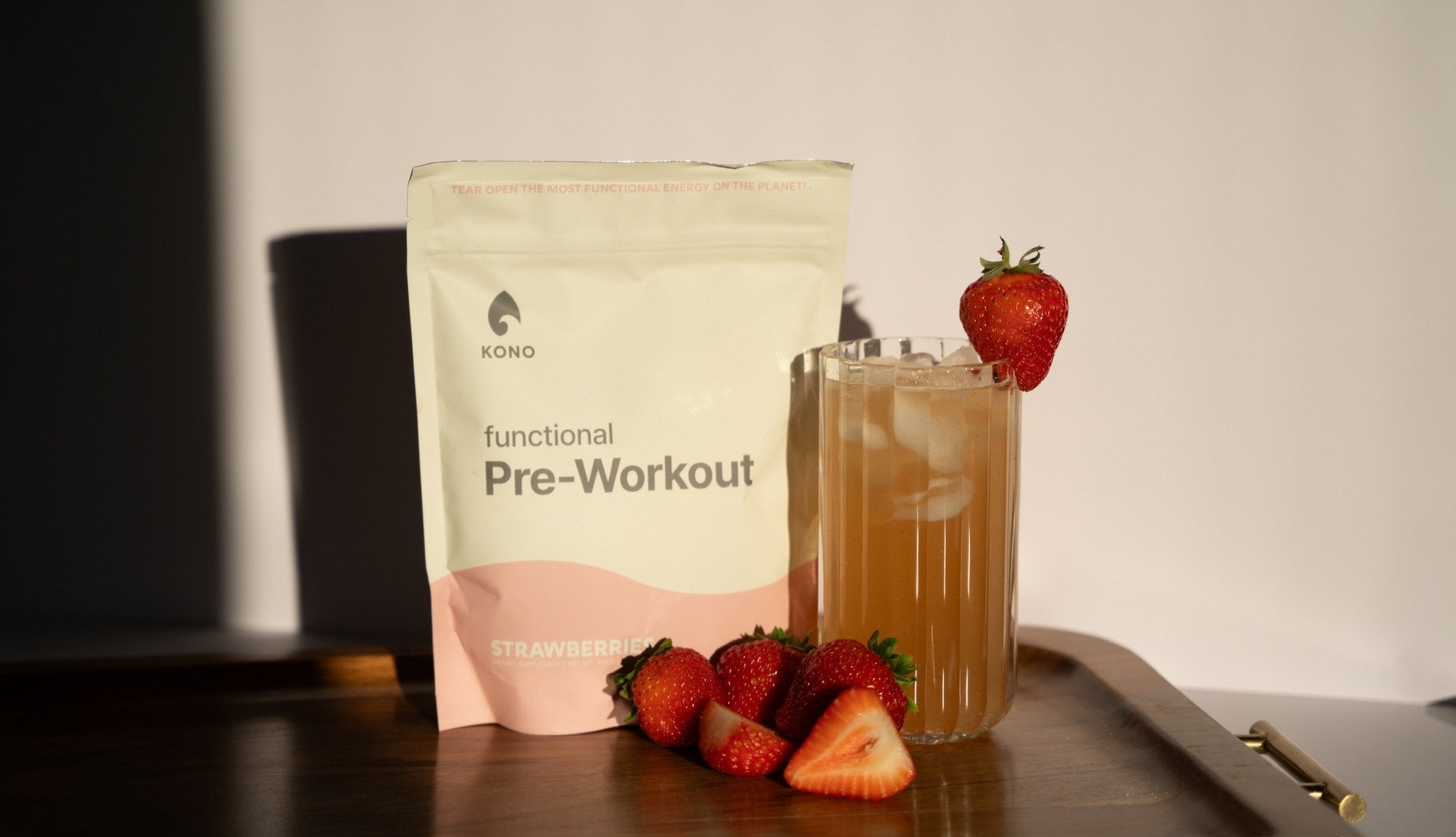 KONO functional pre-workout (strawberries flavor) pouch beside a strawberry-garnished iced drink and fresh strawberries on a wooden tray