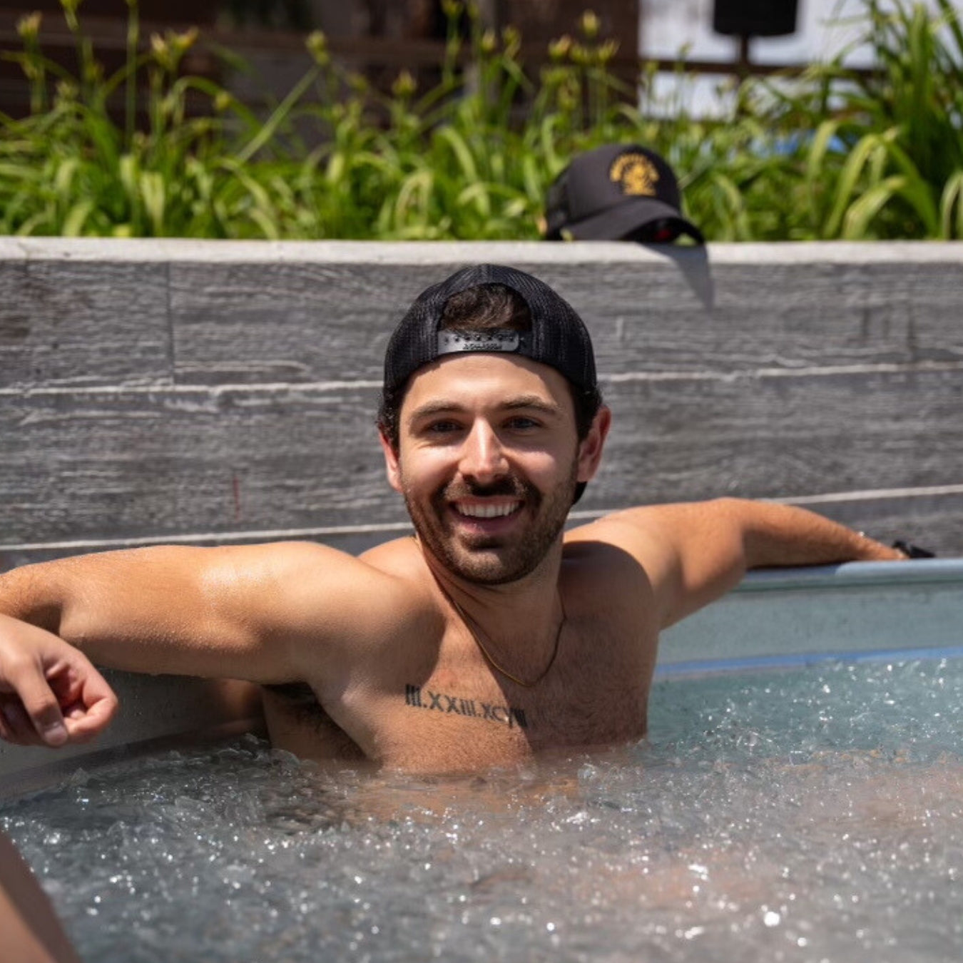 Alex Conley, CEO, smiling in an outdoor cold-plunge pool, arms stretched on the edge, wearing a backward mesh cap.