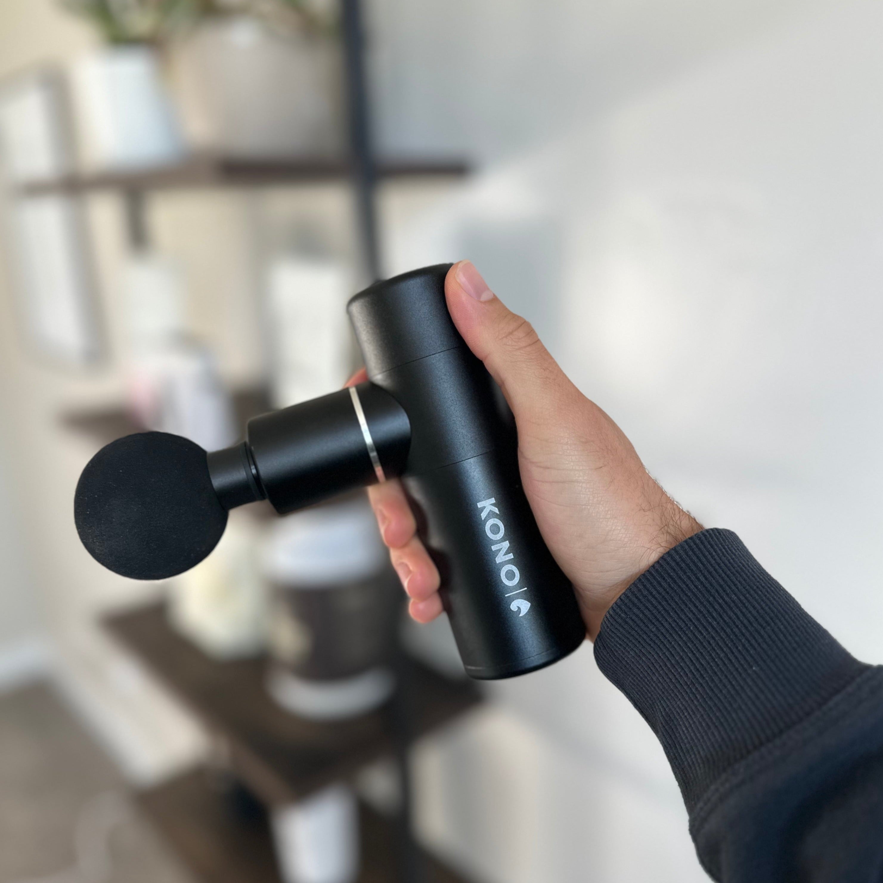 KONO Mini Massage Gun handheld percussion massager—black ball head, shown in hand for scale; portable deep-tissue muscle recovery tool.