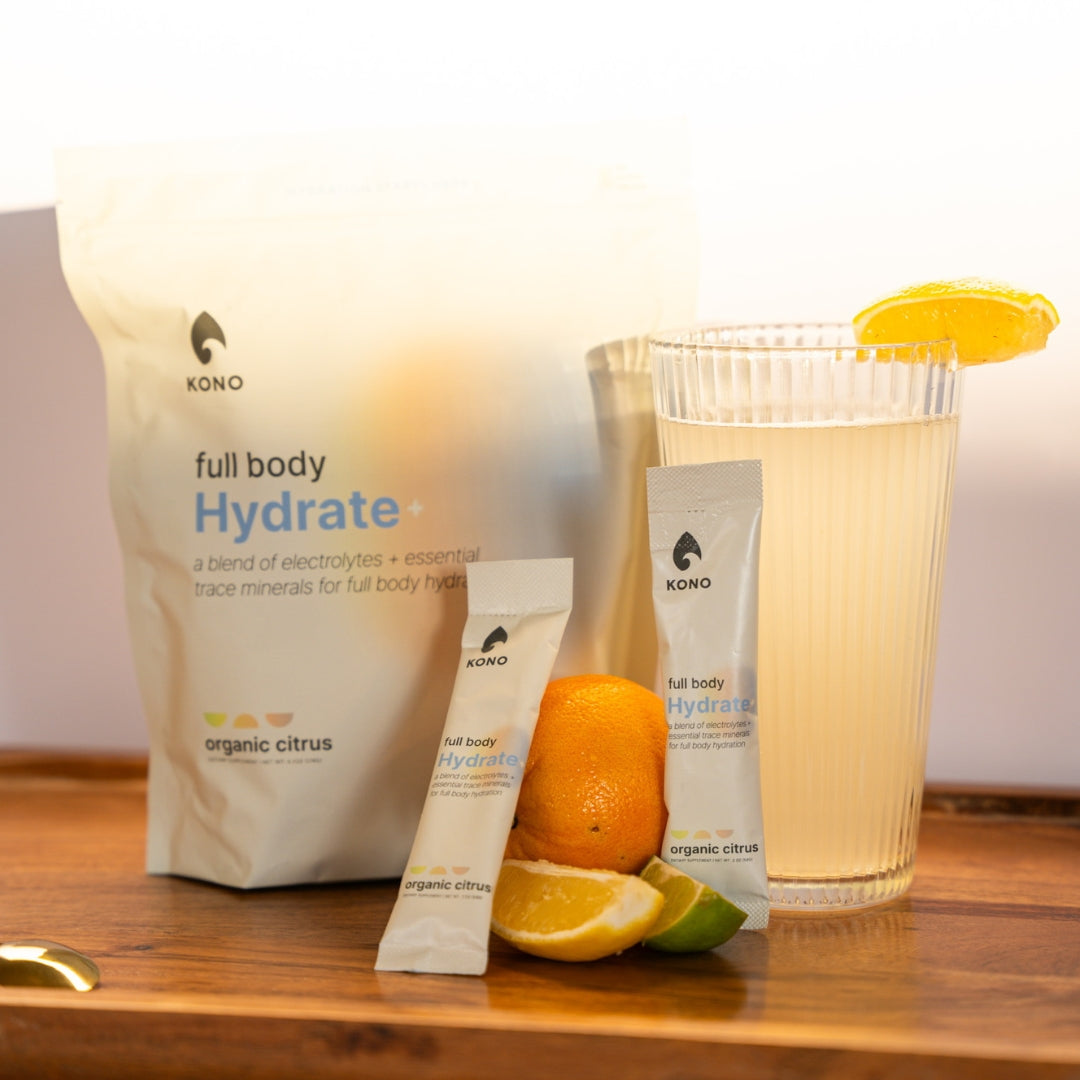 Hand holding KONO full body Hydrate+ organic citrus electrolyte drink mix—resealable pouch, outdoor lifestyle shot