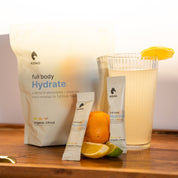 Hand holding KONO full body Hydrate+ organic citrus electrolyte drink mix—resealable pouch, outdoor lifestyle shot