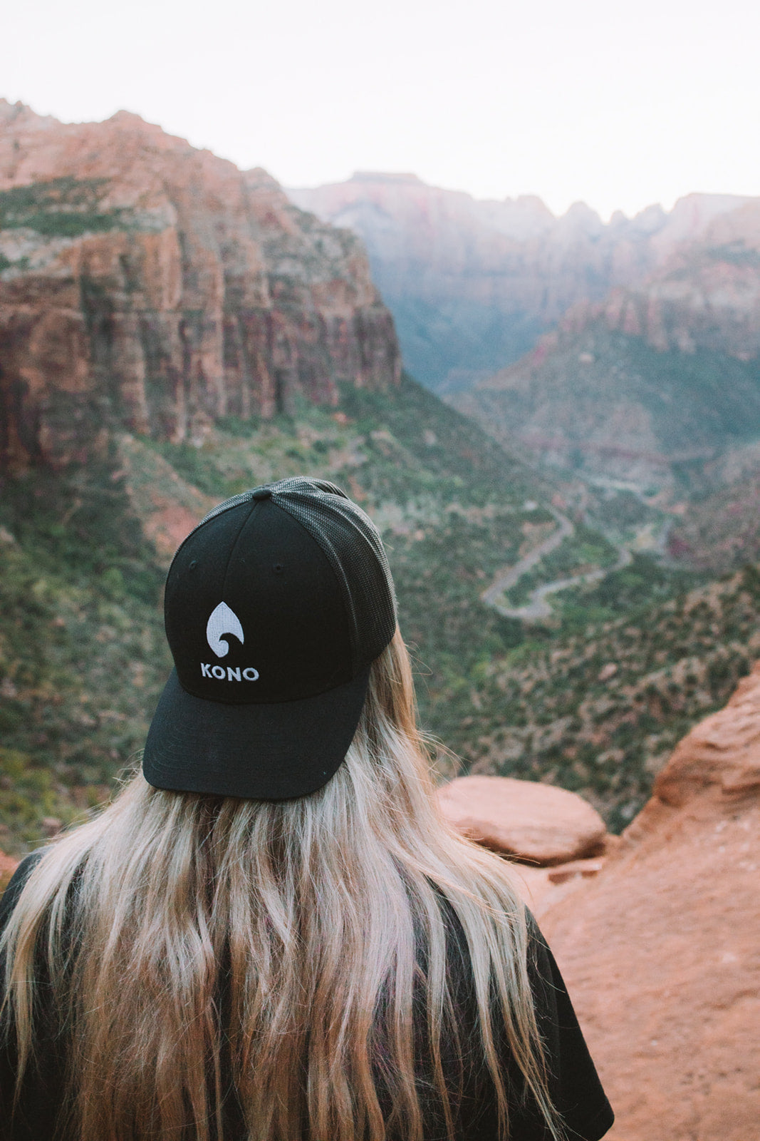 Woman wearing a black KONO embroidered-logo trucker hat overlooking a red-rock canyon—outdoor hiking lifestyle.