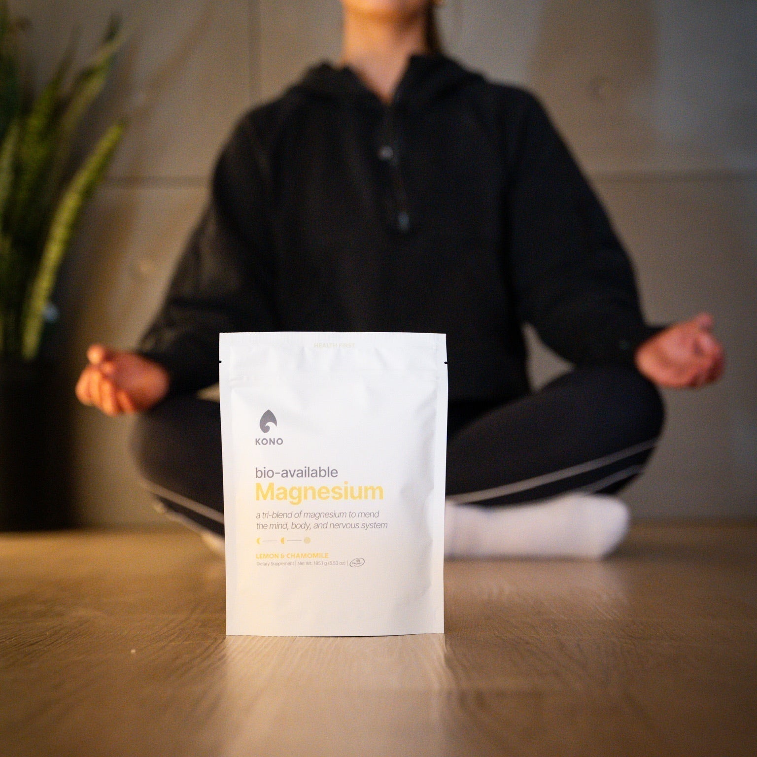 KONO bio-available magnesium pouch (lemon & chamomile) in focus while a person meditates cross-legged in the background