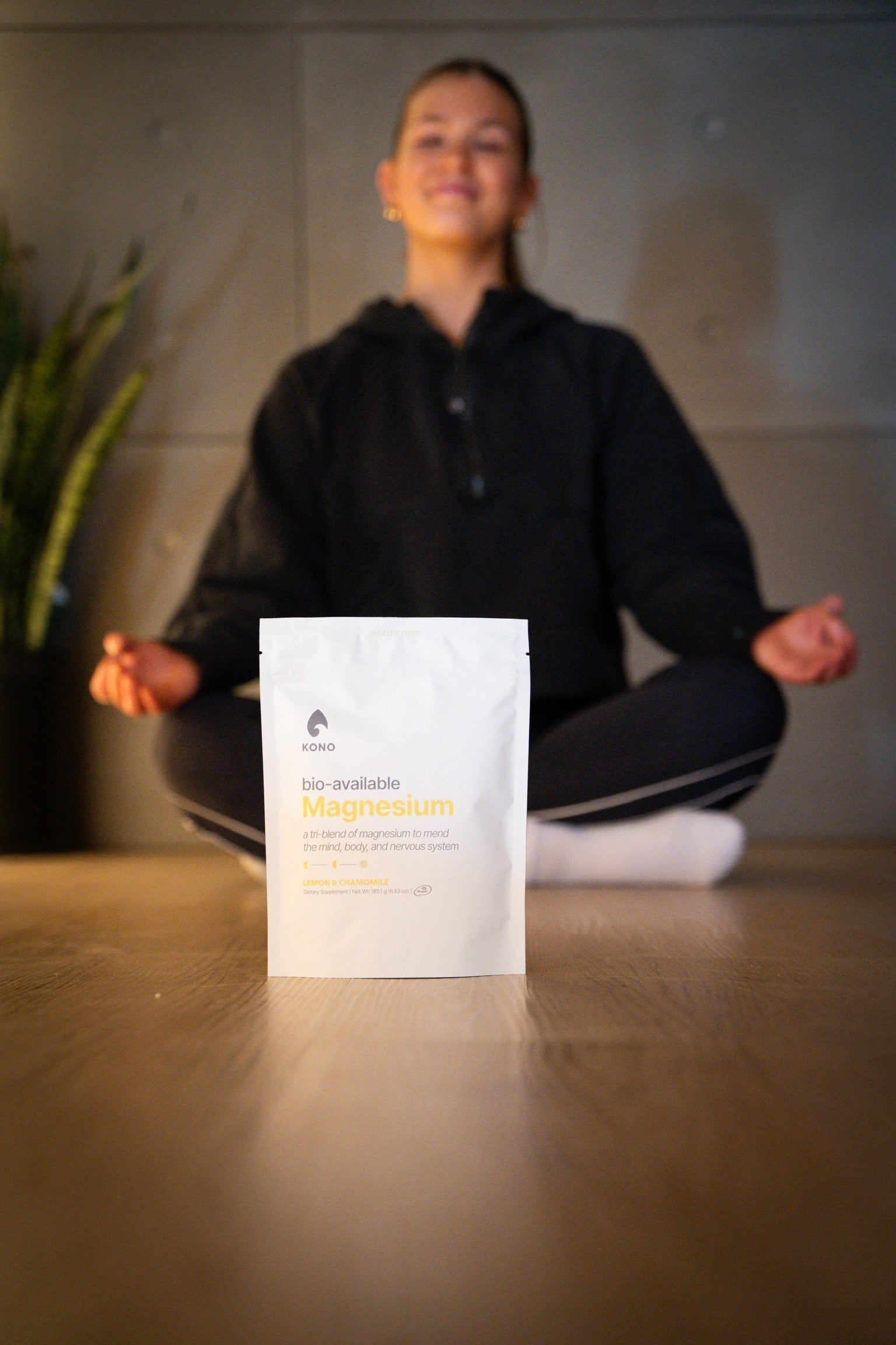 KONO bio-available magnesium pouch (lemon & chamomile) in focus while a person meditates cross-legged in the background
