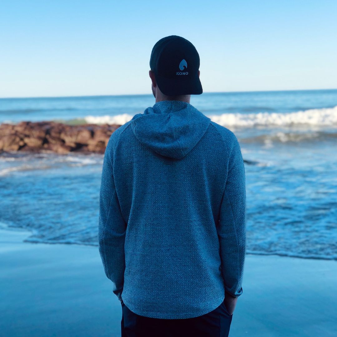 peaceful coastal scene—individual standing near shoreline with rocks and calm surf