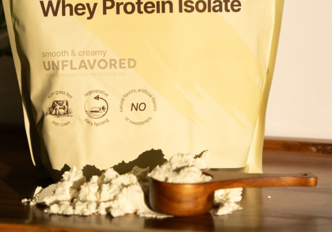 close-up of KONO regenerative grass-fed whey protein isolate (unflavored) pouch with wooden scoop and spilled powder on a tray in warm light