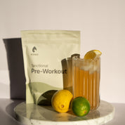 KONO Functional Pre-Workout Lemons & Limes—pouch with an iced pre-workout drink and lemon/lime on a marble pedestal.