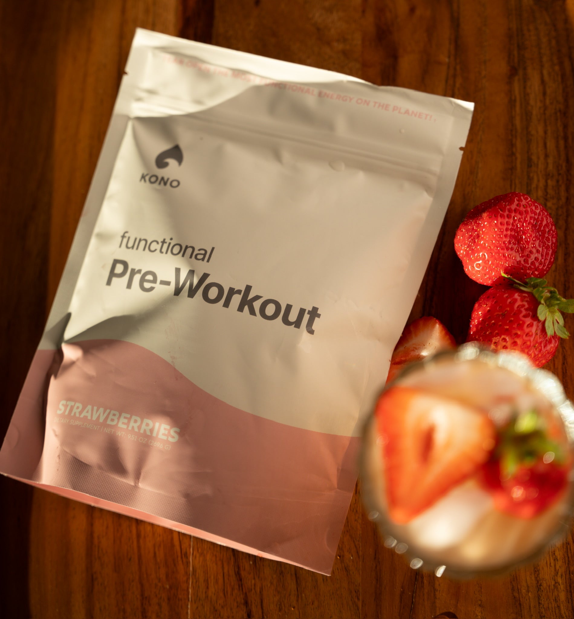 KONO functional pre-workout strawberries flavor pouch on a wooden table with fresh strawberries and iced drink