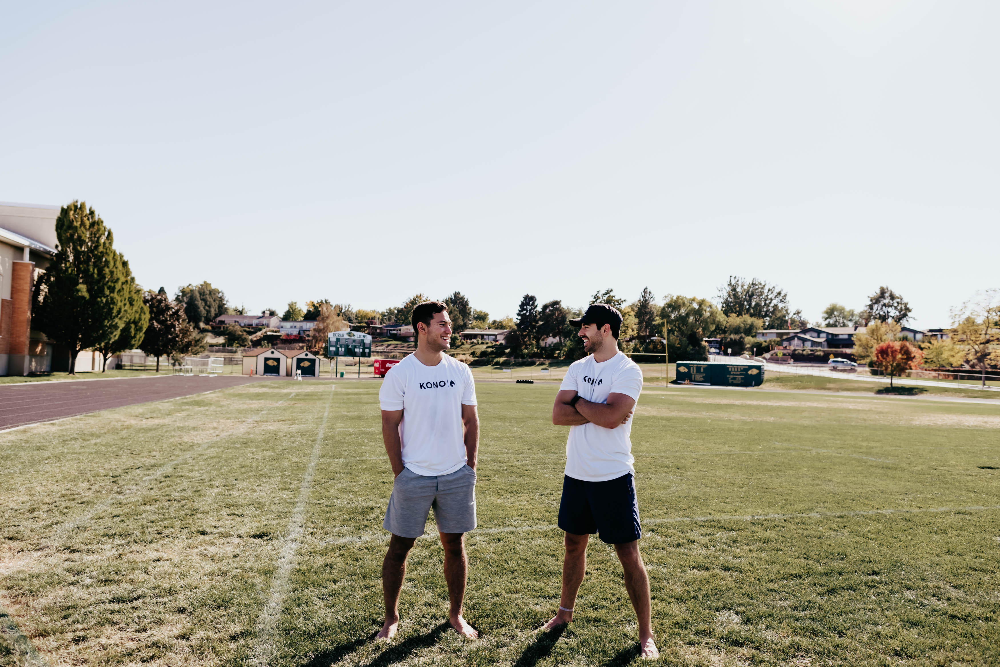 fitness lifestyle photo—two men in athletic shorts and KONO tops on a track and field complex