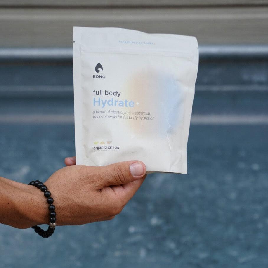 KONO full body Hydrate+ organic citrus electrolyte powder with trace minerals—pouch, single-serve sticks, and lemon-garnished glass.
