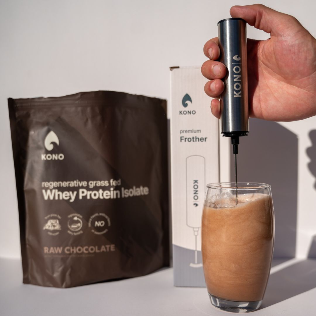 KONO premium handheld frother mixing a chocolate whey protein shake—next to KONO Whey Protein Isolate Raw Chocolate pouch and frother box.