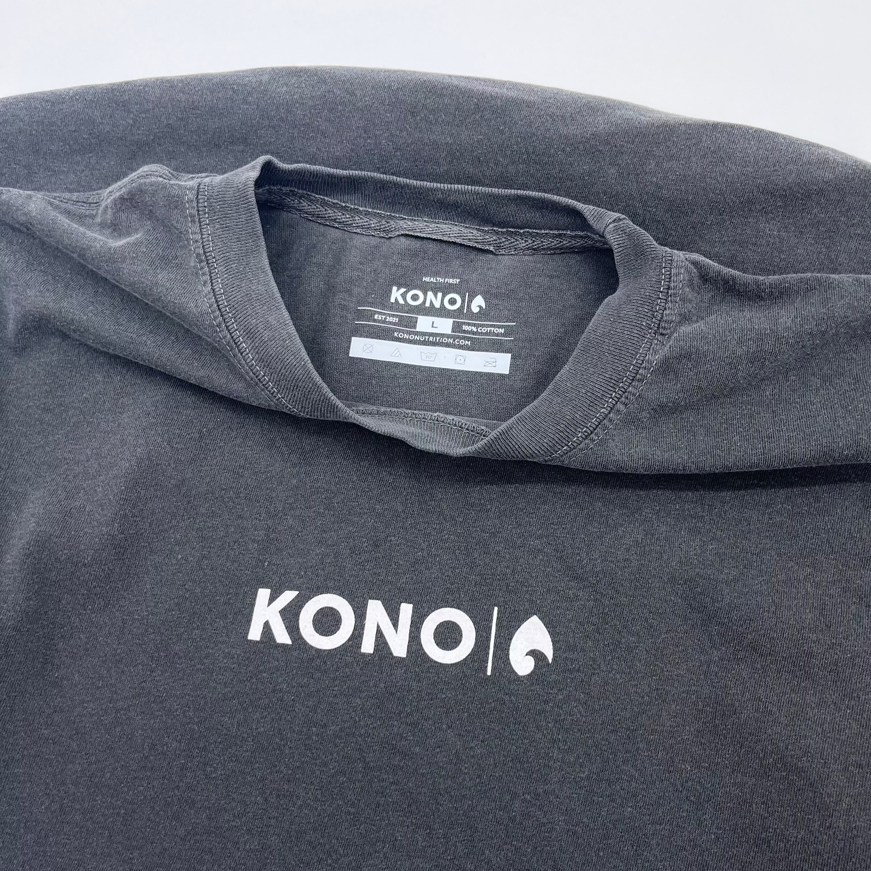 Close-up flat lay of charcoal KONO tee—front logo and inside neck label (100% cotton, size L)