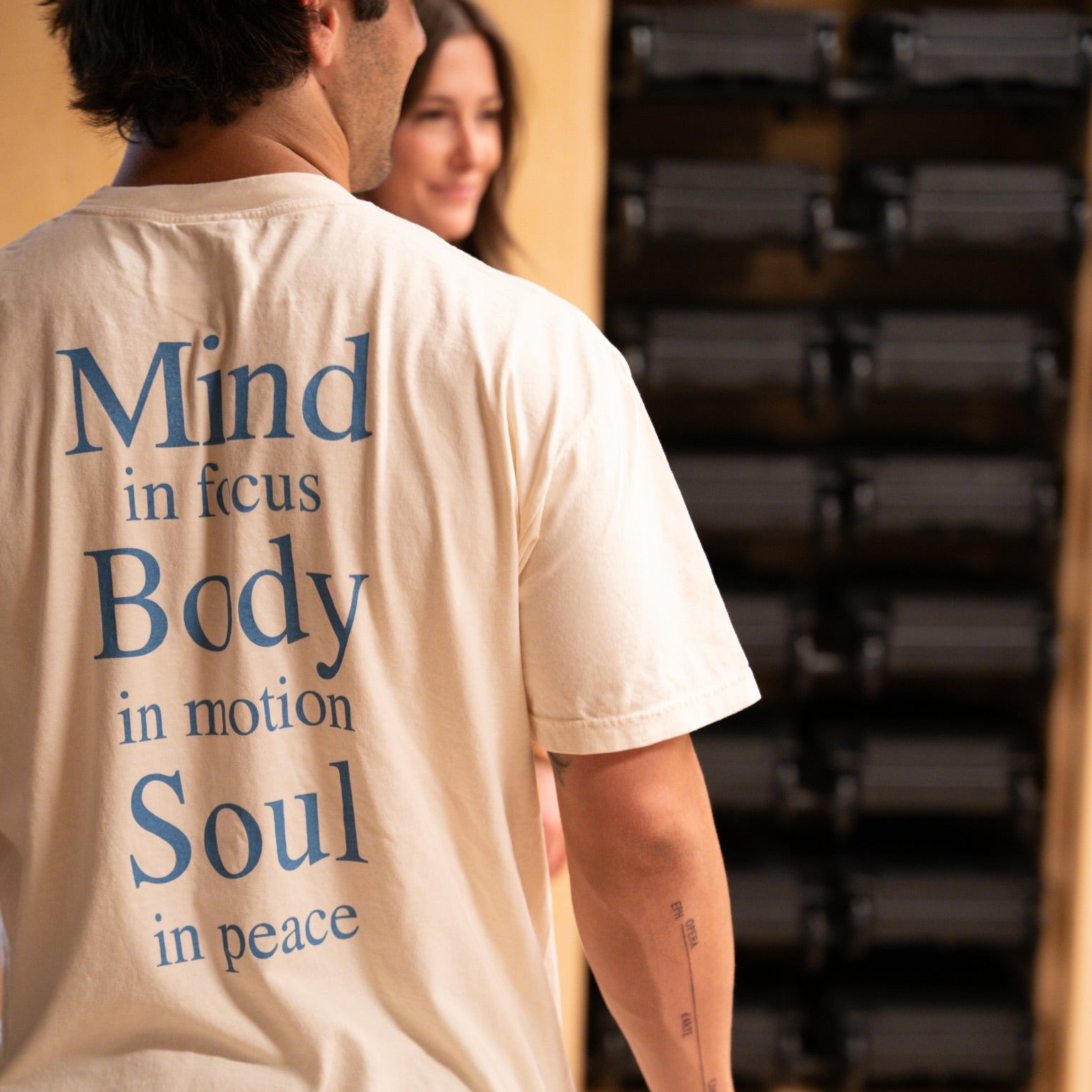 Close back of cream KONO t-shirt with blue ‘Mind in focus, Body in motion, Soul in peace’ print—fitness lifestyle scene.