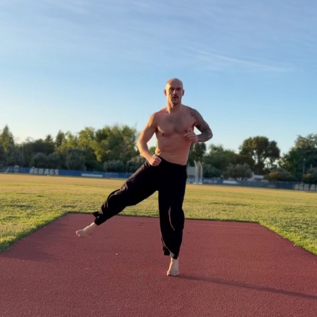 Man performing a barefoot balance and stability movement on a track field at sunset
