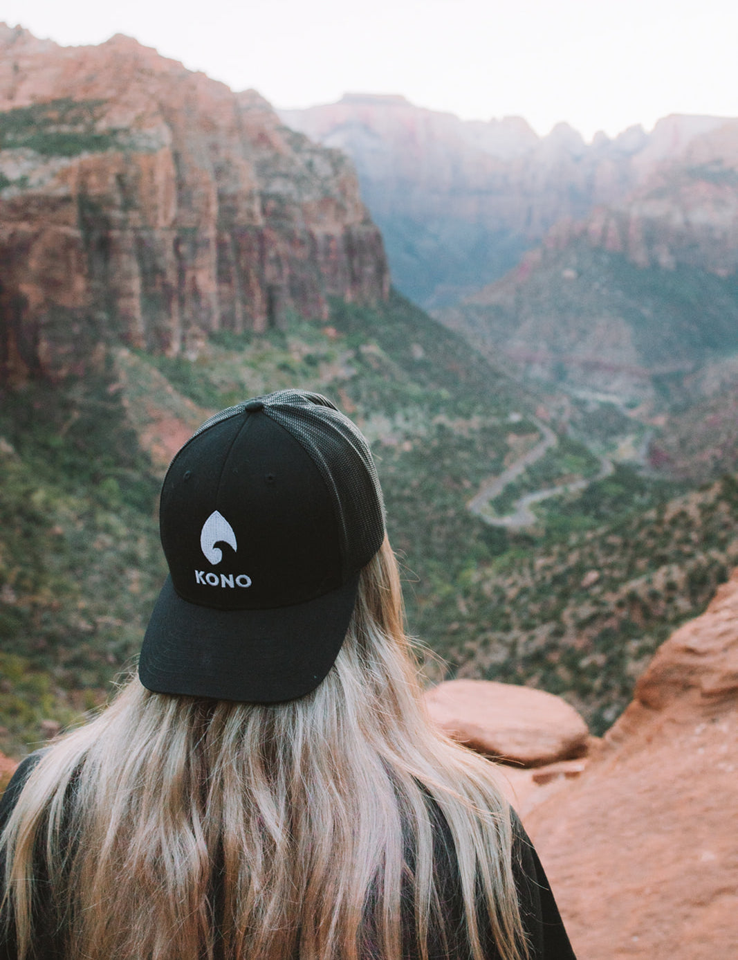 Woman wearing a black KONO embroidered-logo trucker hat overlooking a red-rock canyon—outdoor hiking lifestyle.